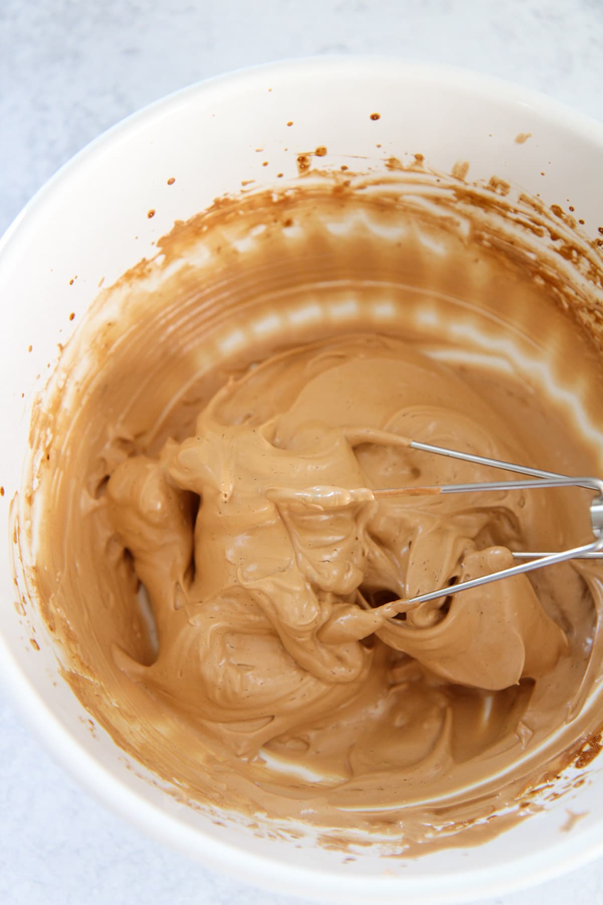 light brown whipped coffee in a white bowl with a metal whisk.