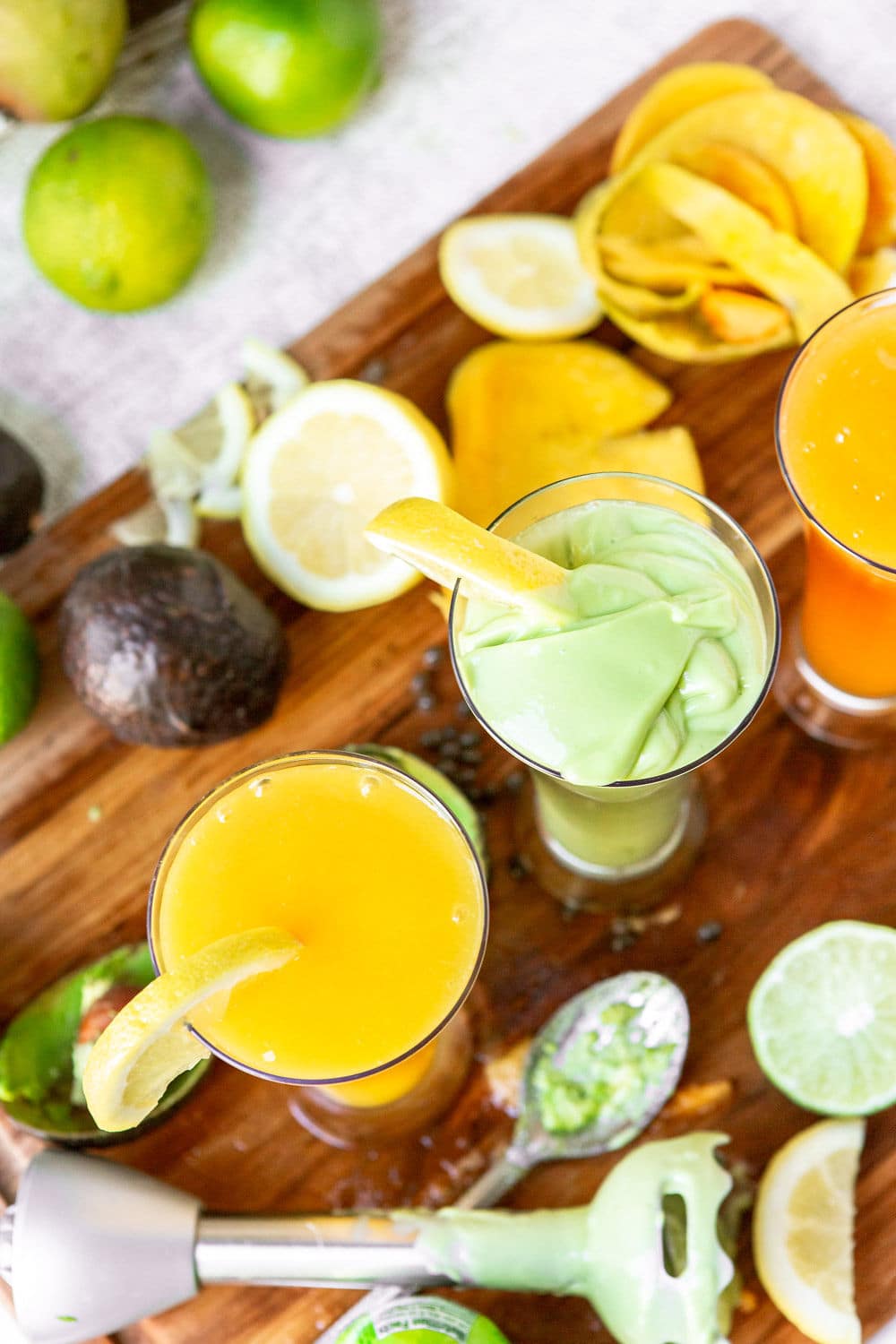 two glasses filled with a green and yellow juice with an immersion blender on the side. 