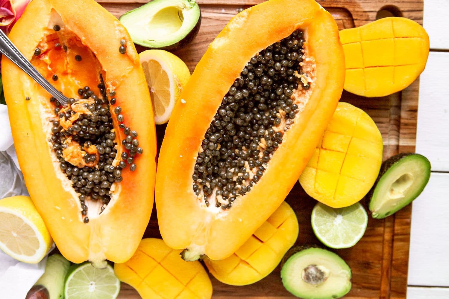 a papaya cut in half with avocados and mangoes on the side. 