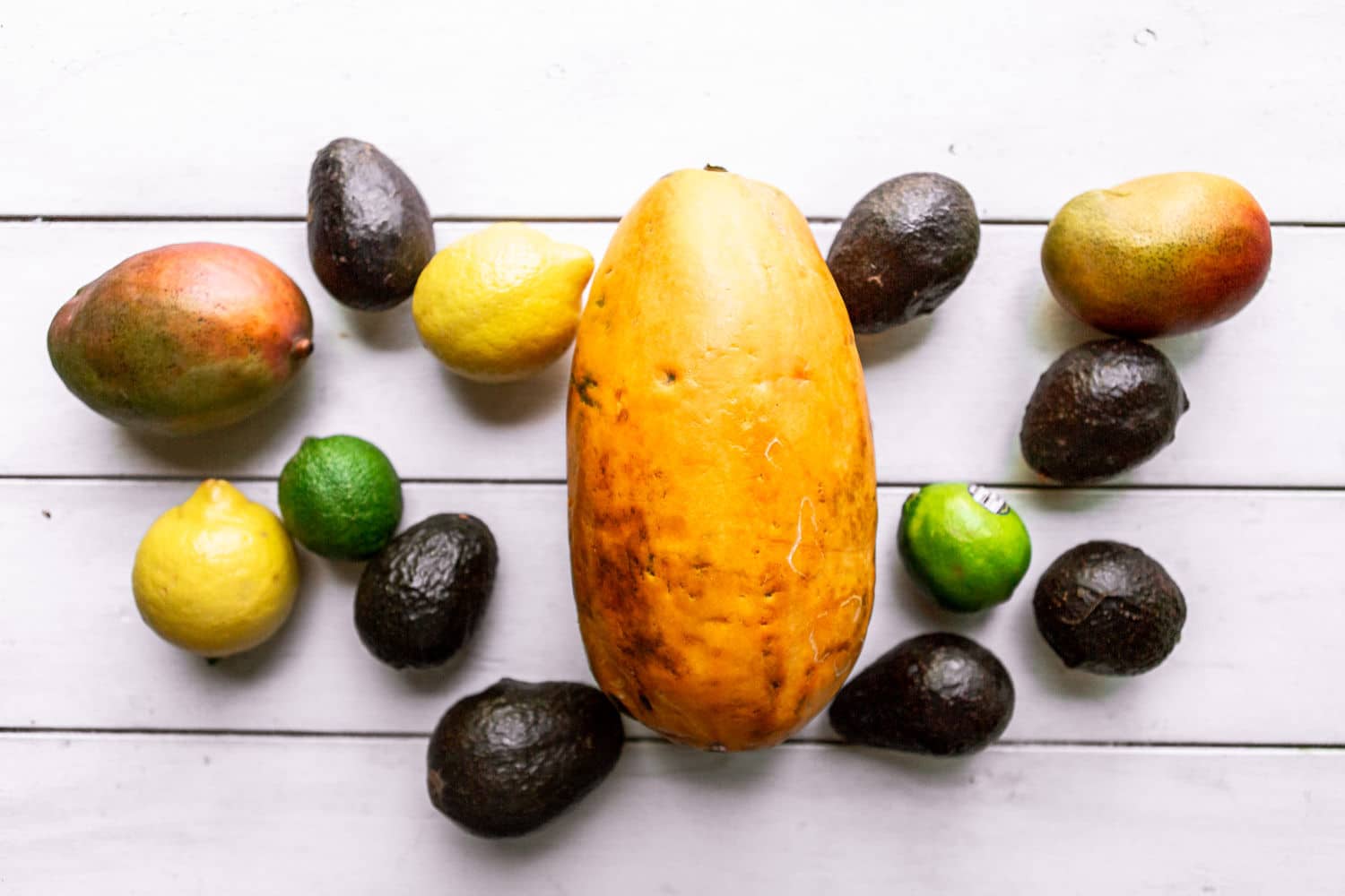 papaya, mangoes, avocados, lemons, and limes on a white surface.