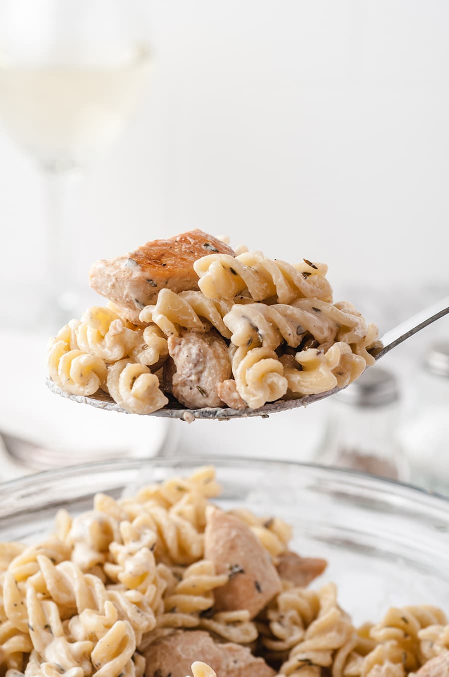 a spoon lifting pasta and chicken out of a bowl. 