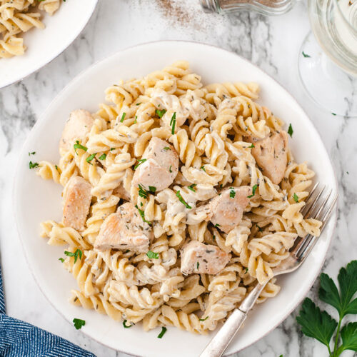 chicken and pasta in a white bowl with a fork and a blue towel on the side.