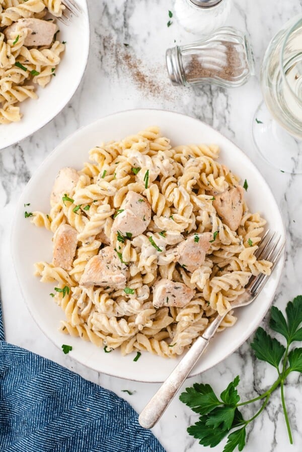chicken and pasta in a white bowl with a fork and a blue towel on the side.