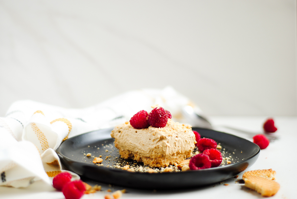 a horizontal up close shot of a slice of dalgona cheesecake on a black plate with crushed cookies and raspberries. 