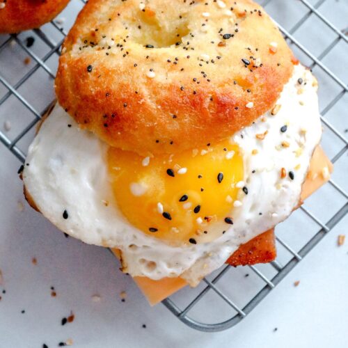 a keto breakfast sandwich with a sunny side up egg, everything bagel, and cheese on a wire rack.