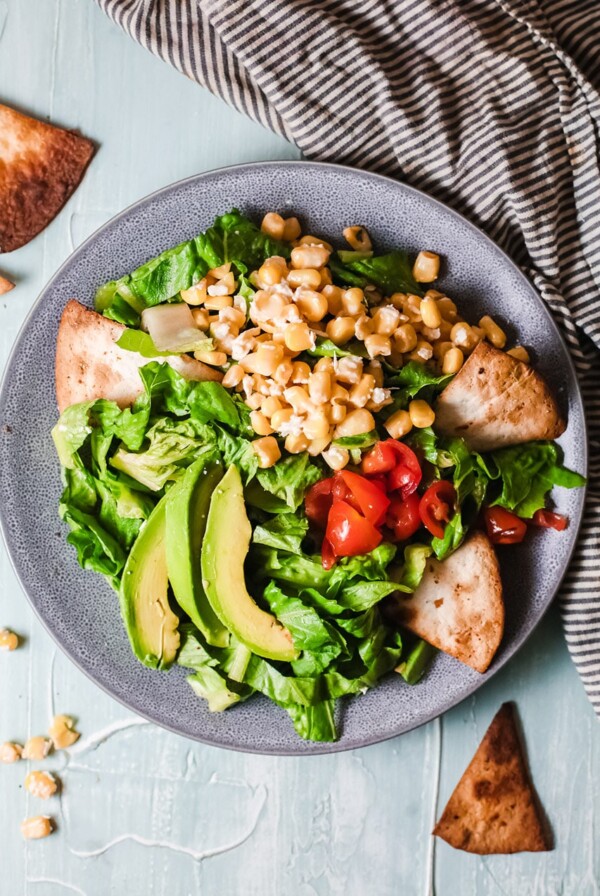 lettuce, corn, avocado, and tortilla chips in a blue bowl with a black and white striped towel on the side.