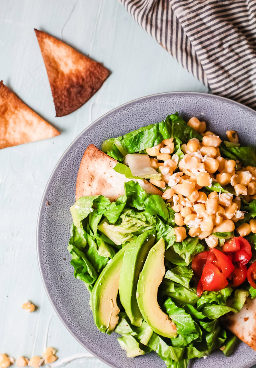 a blue bowl with lettuce, avocado, Mexican corn salad, tomatoes and tortilla chips on the side. 