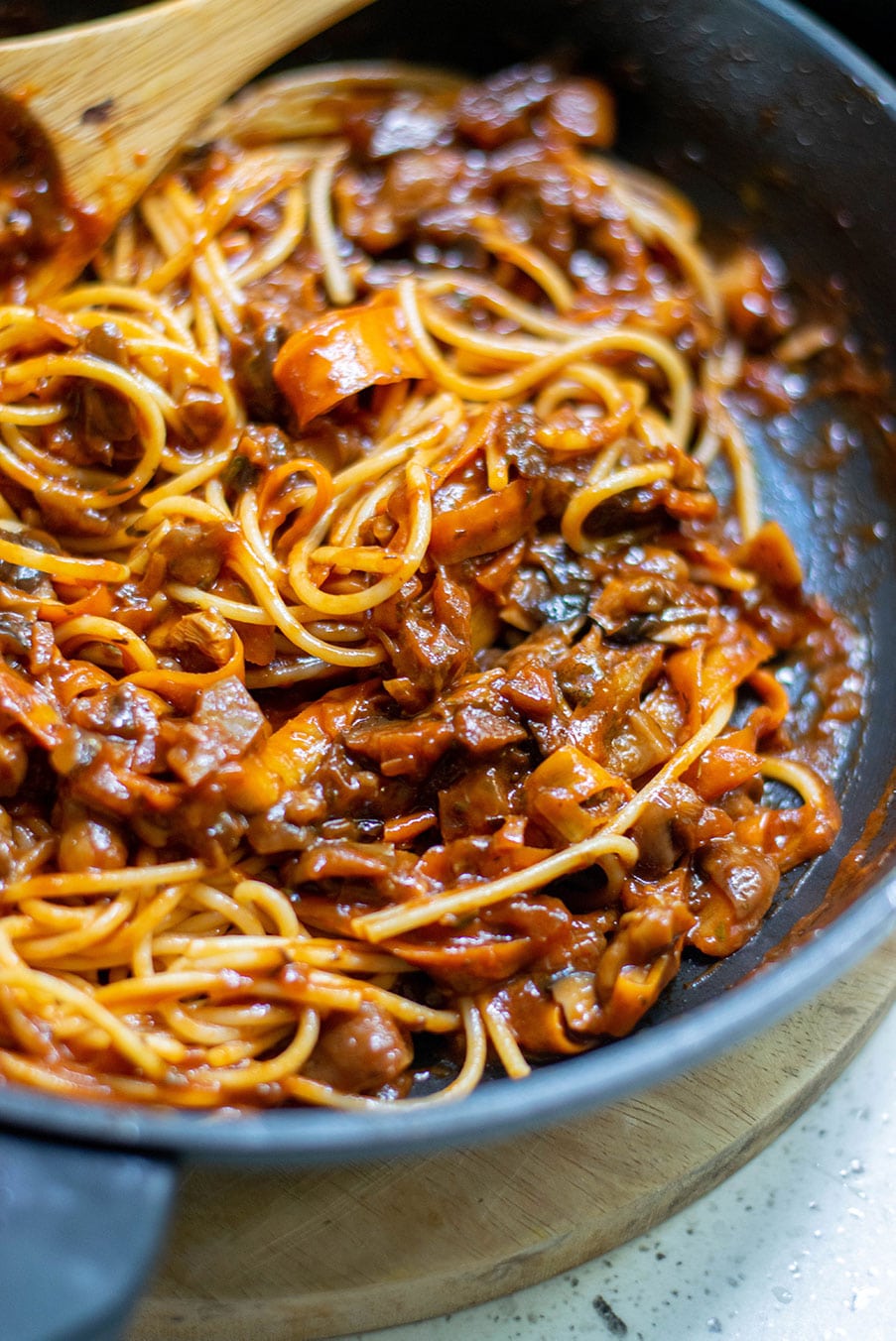 up close shot of spaghetti and mushroom bolognese sauce with a wooden spoon inside a black skillet. 