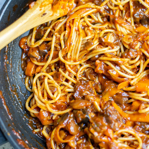 mushroom bolognese with pasta and a wooden spoon in a black skillet.