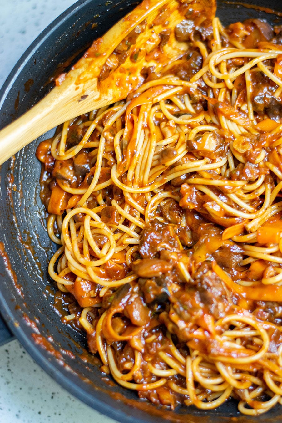 mushroom bolognese with pasta and a wooden spoon in a black skillet. 