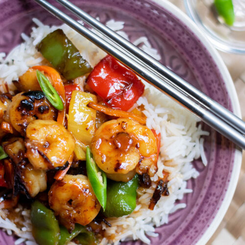 sweet and sour shrimp over white rice in a purple bowl with chop sticks on top.