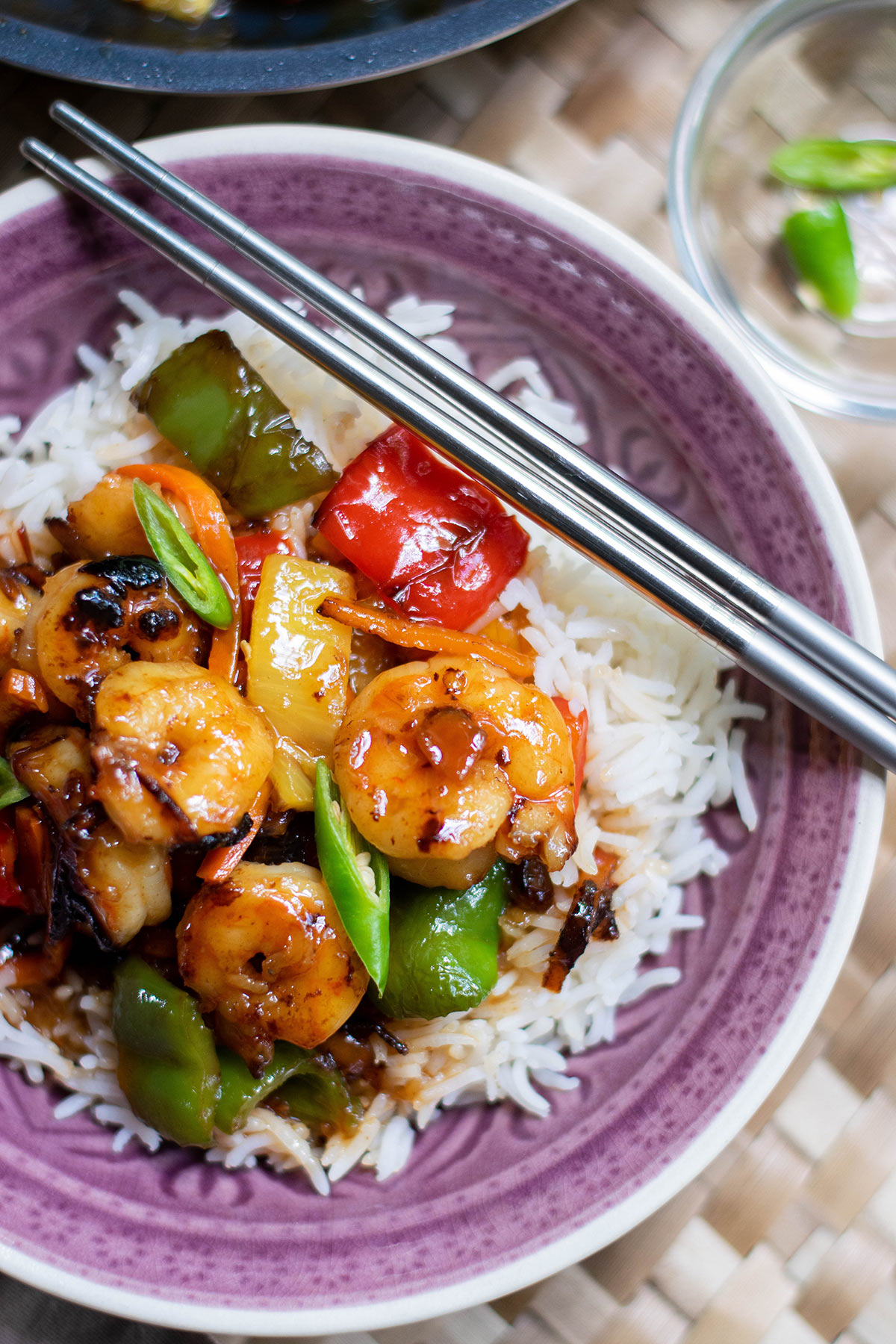 sweet and sour shrimp over white rice in a purple bowl with chop sticks on top.