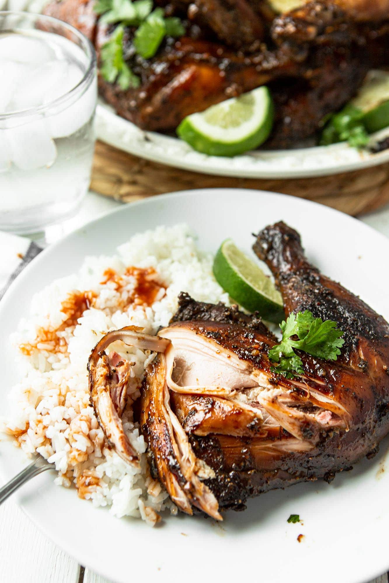 a chicken leg quarter with lime, cilantro, white rice and sauce on top of the rice. 