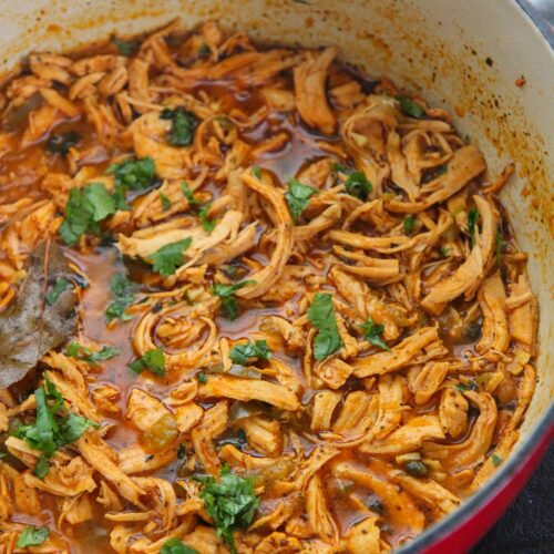 latin shredded chicken stew with cilantro on top in a red dutch oven.