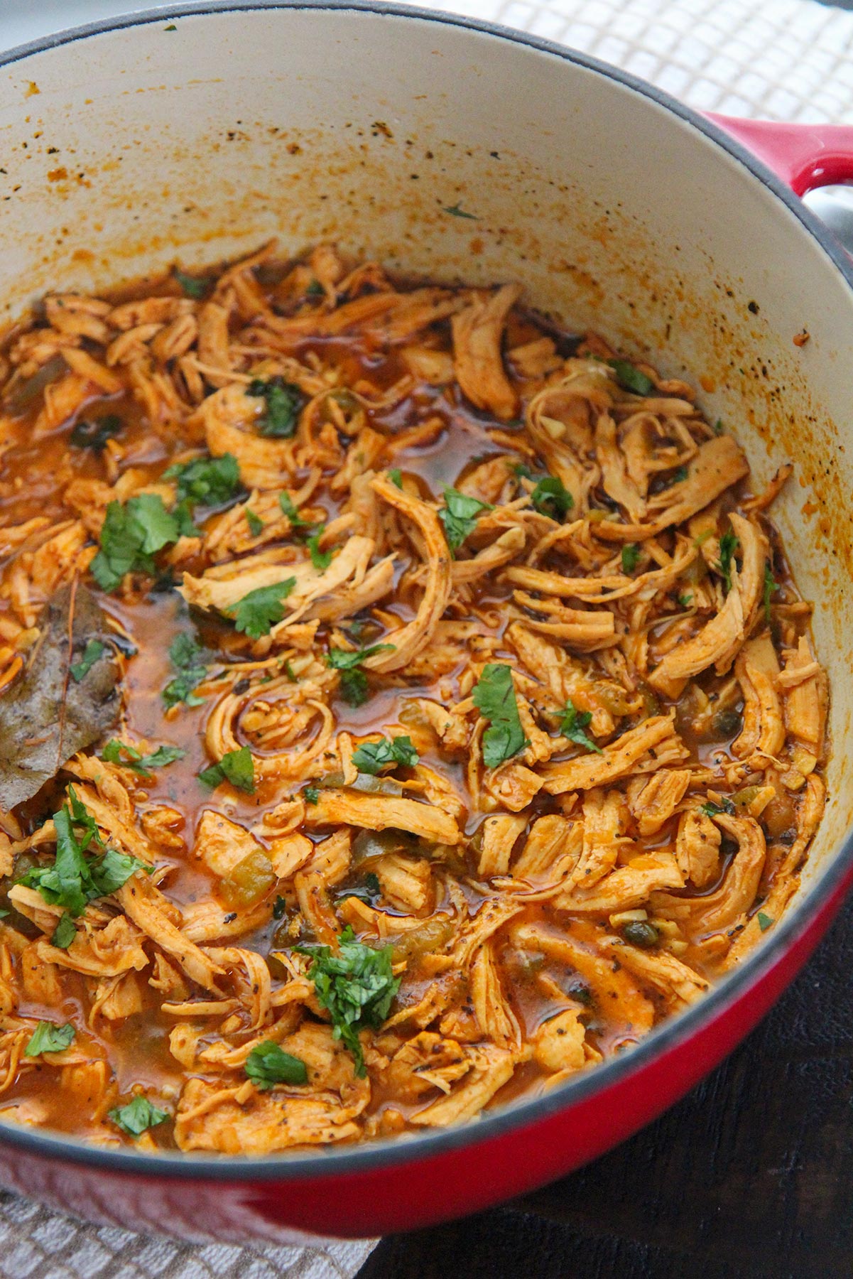 latin shredded chicken stew with cilantro on top in a red dutch oven. 