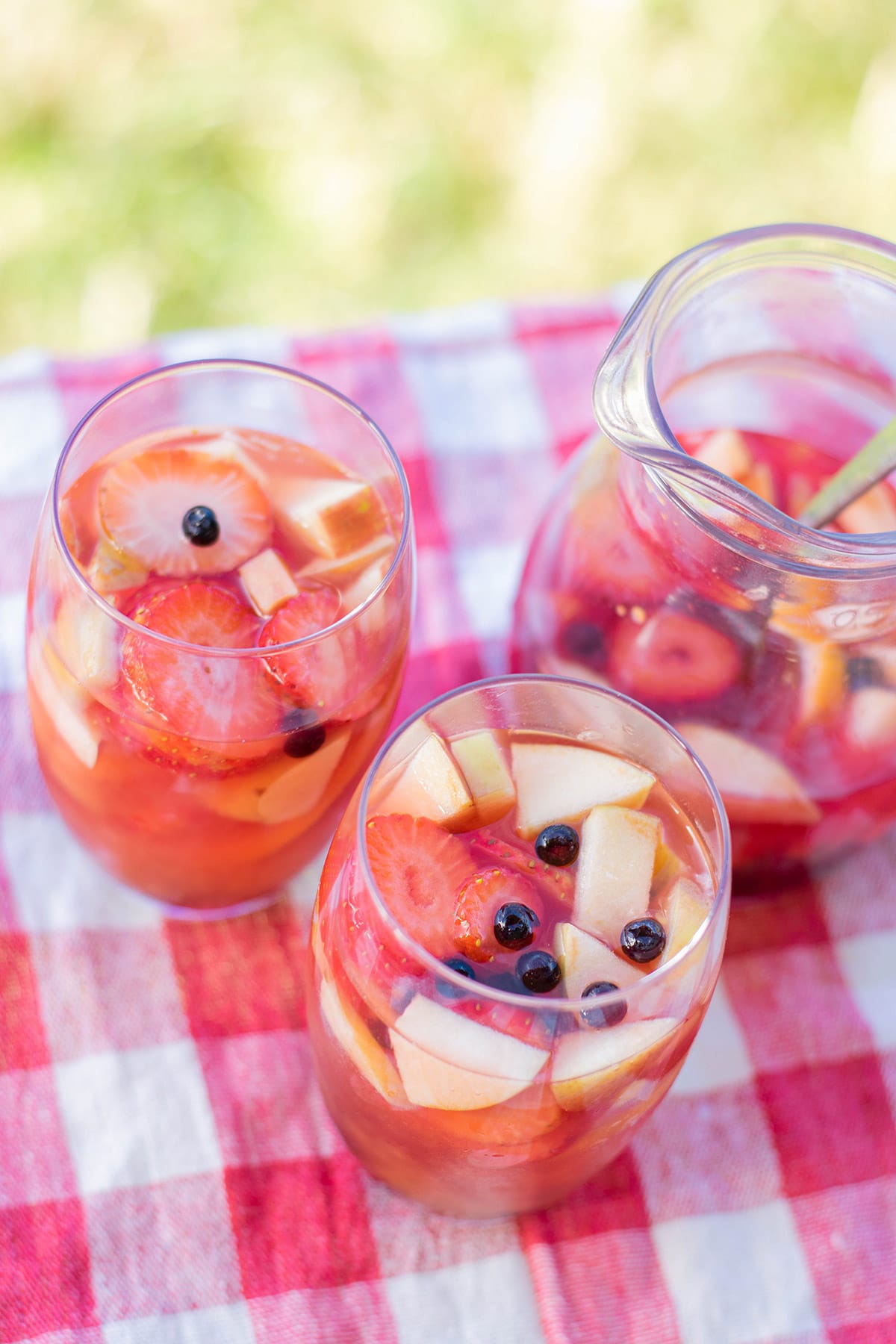 two glasses filled with mango sangria on a picnic table outside. With a pitcher in the background filled with sangria. 