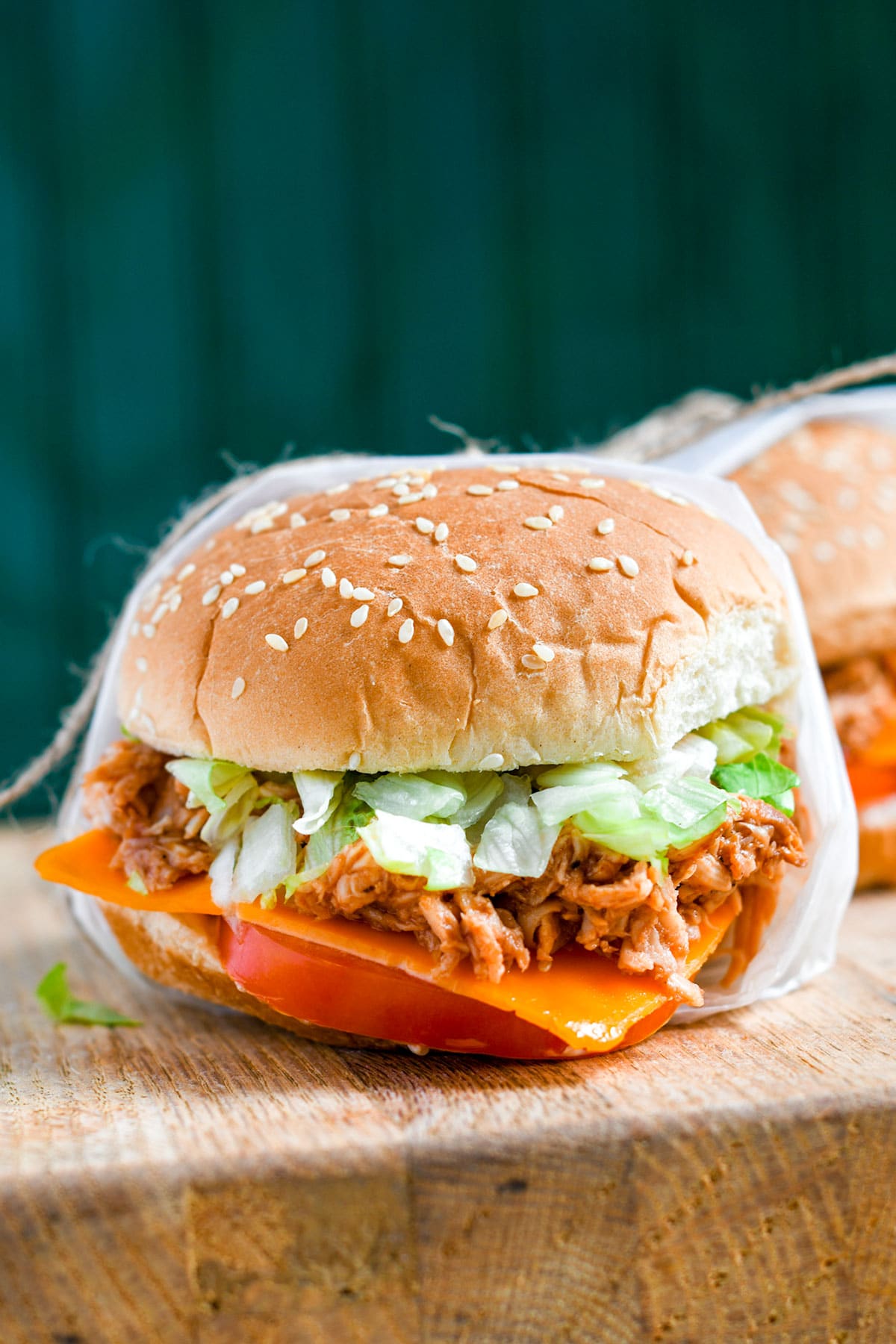 a shredded chicken sandwich on a wooden board and a green backdrop.