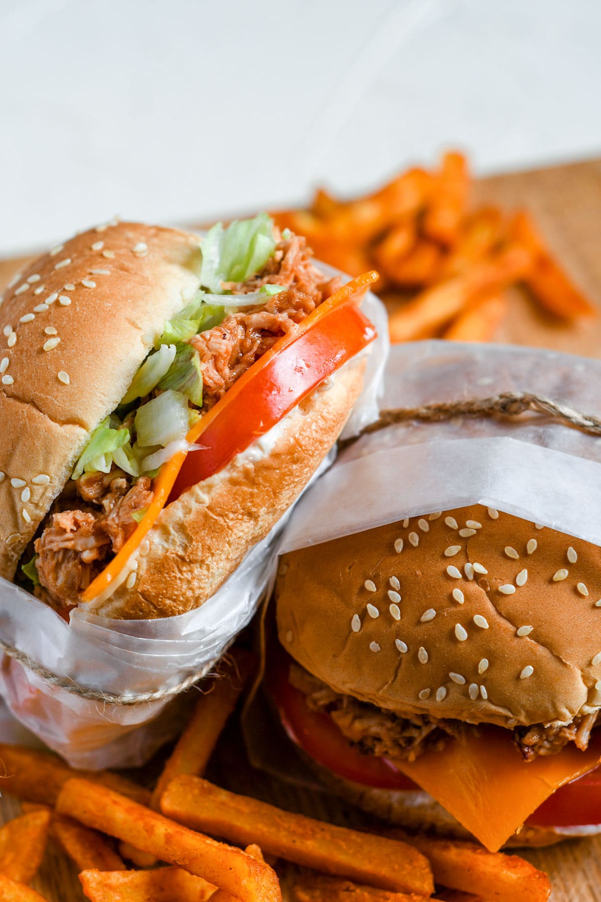 two shredded chicken sandwiches with lettuce, tomato, cheese, and sweet potato fries on the side. 