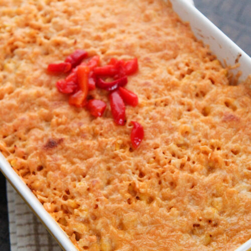 arroz imperial in a yellow casserole dish with melted yellow cheese and red peppers on the center.