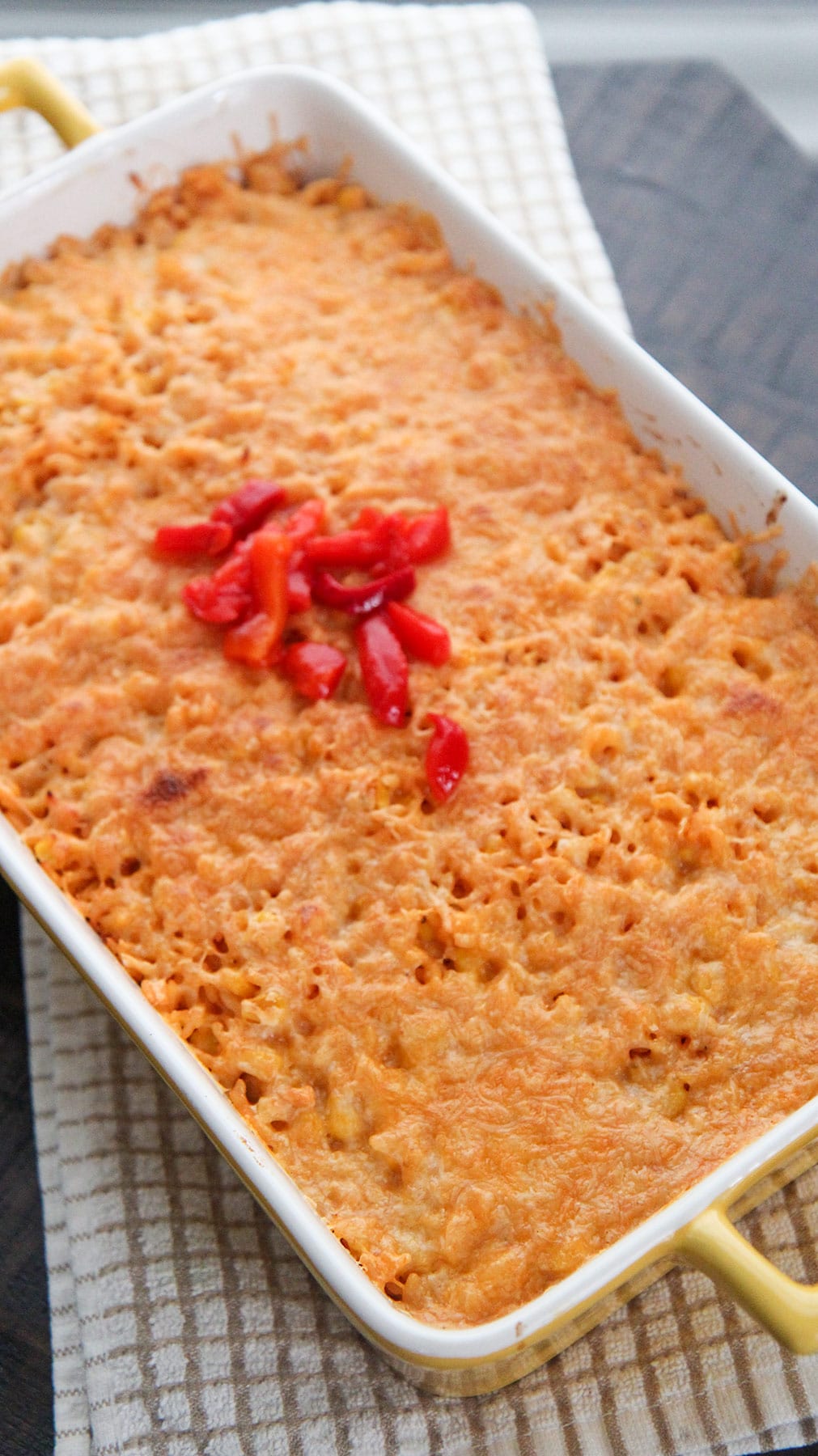 arroz imperial in a yellow casserole dish with melted yellow cheese and red peppers on the center. 