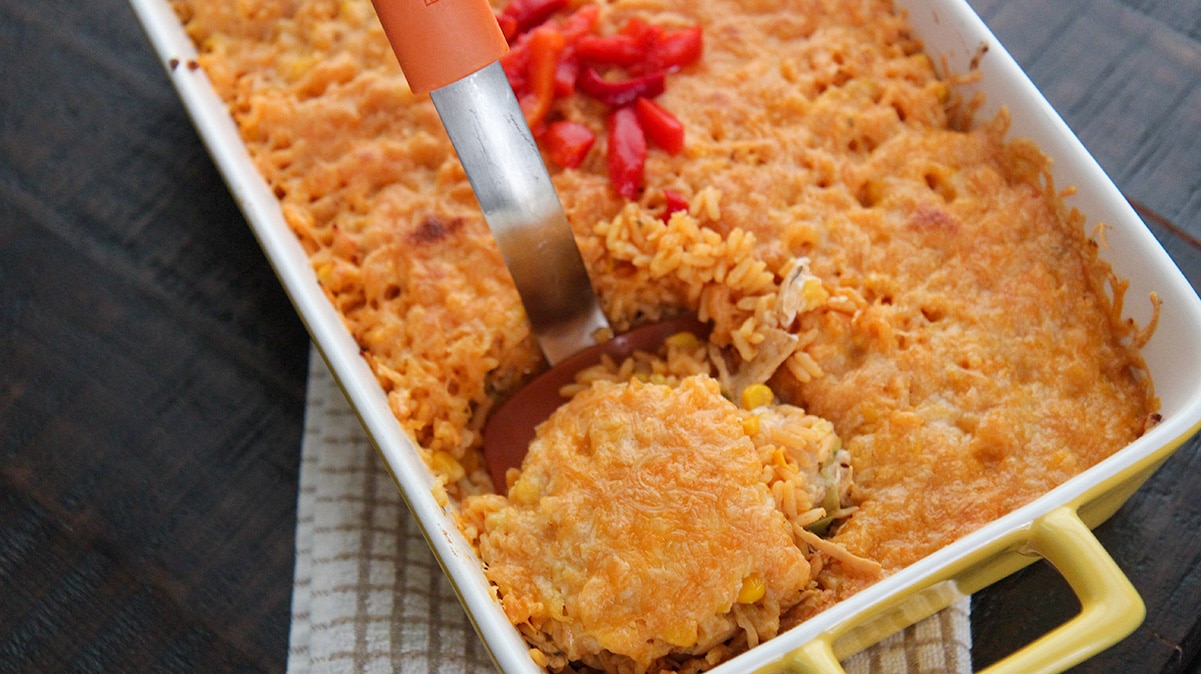 a casserole of imperial rice with an orange spatula lifting a portion out of the casserole. 