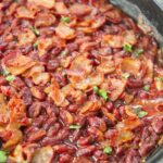 chipotle baked beans in an iron skillet with bacon and parsley on top.