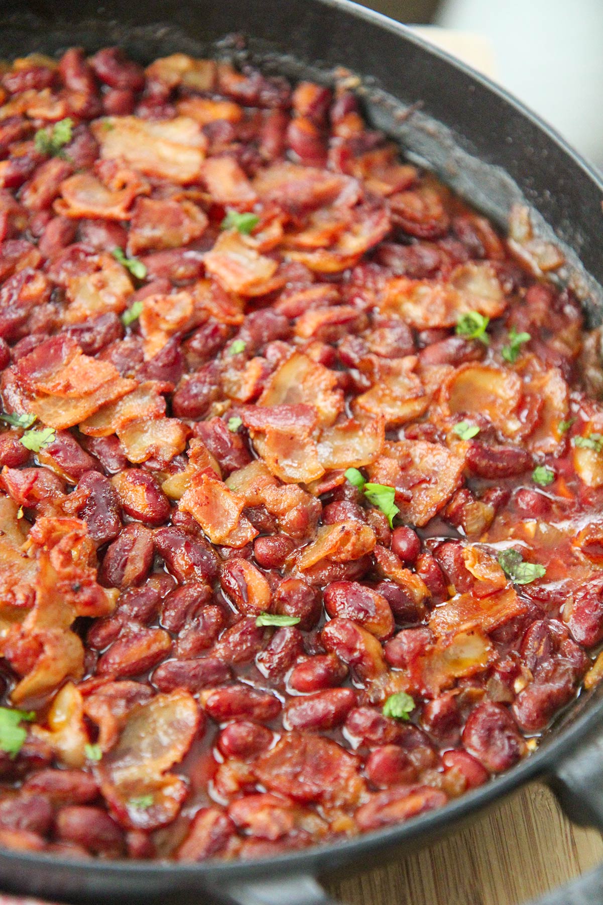 chipotle baked beans in an iron skillet with bacon and parsley on top. 