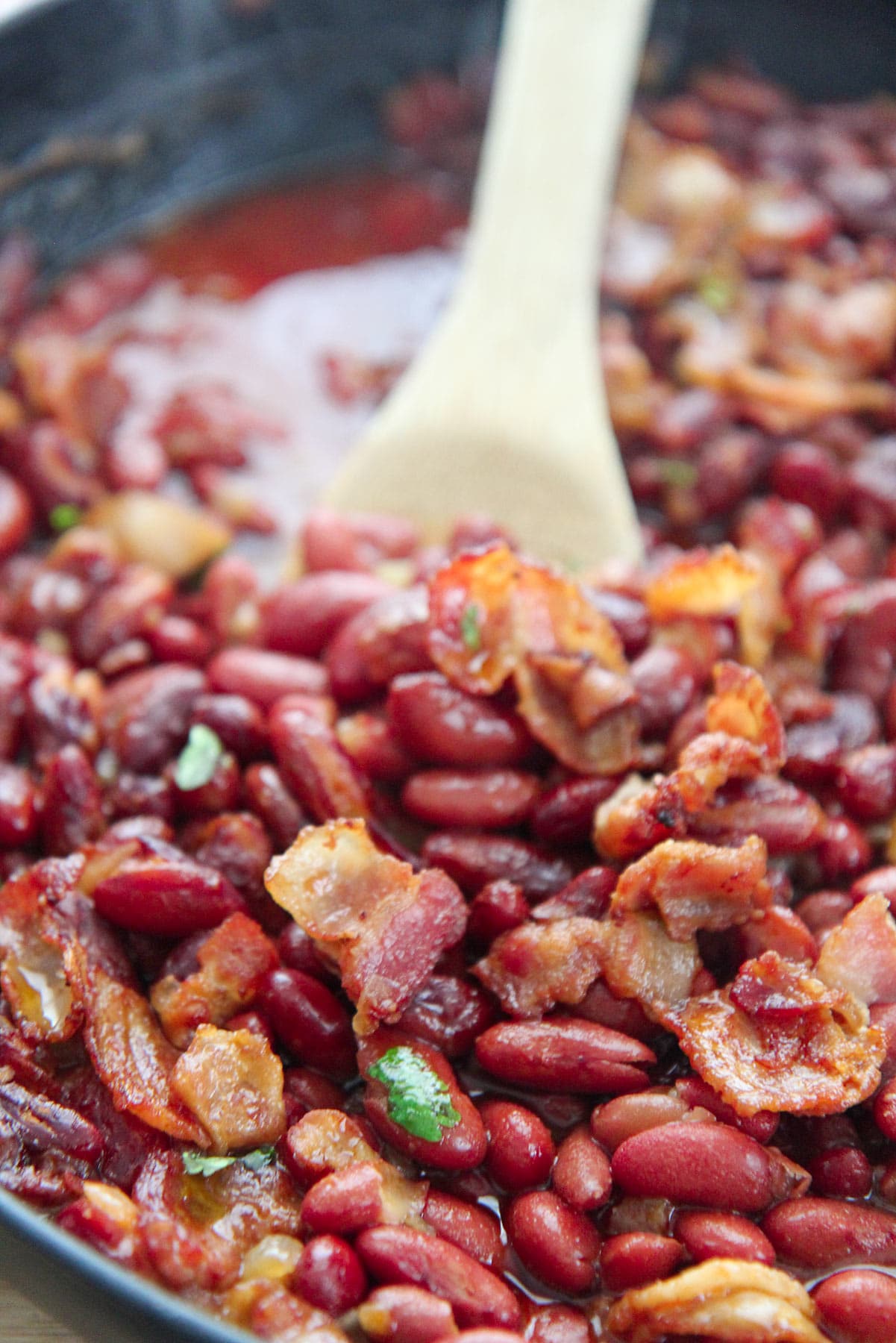 baked beans in a cast iron skillet with a wooden spoon.