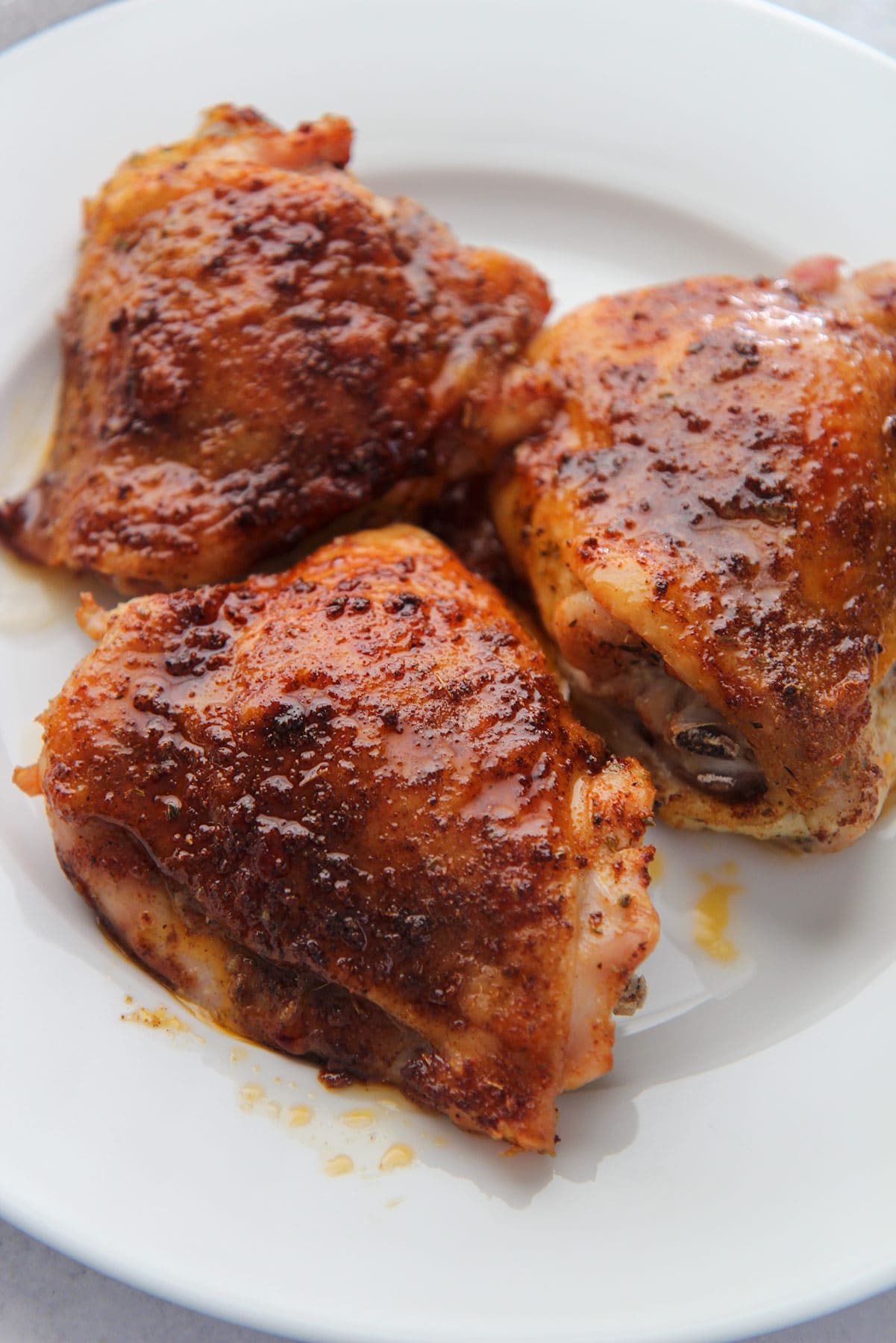 three crispy colorful chicken thighs on a white plate up close. 