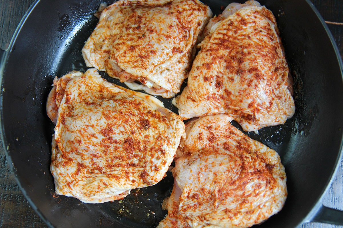 four raw chicken thighs seasoned in a cast iron skillet. 