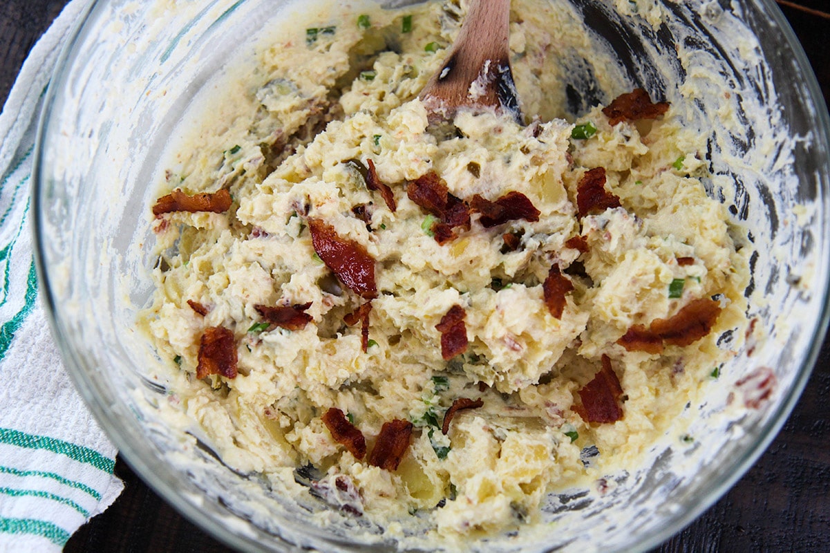 potato salad with bacon in a glass bowl and a towel on the side. 