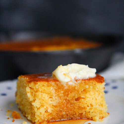 a slice of cornbread with butter and honey on a plate.