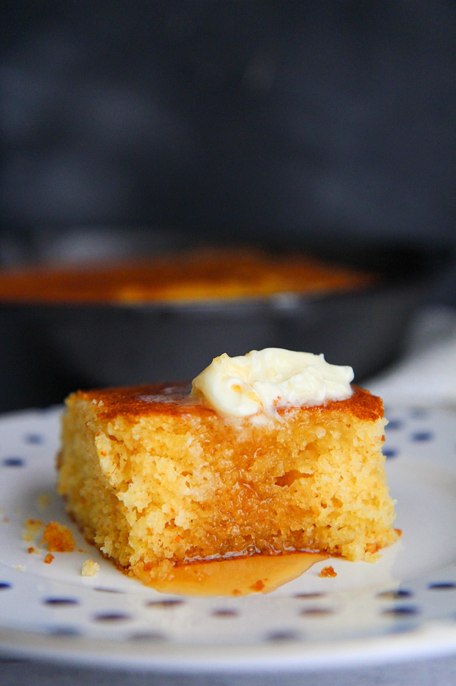 a slice of cornbread with butter and honey on a plate.