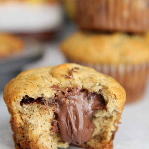 Nutella stuffed banana muffin up close with a nutella jar and more muffins in the background.