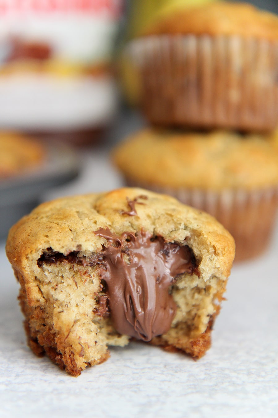 Nutella stuffed banana muffin up close with a nutella jar and more muffins in the background.