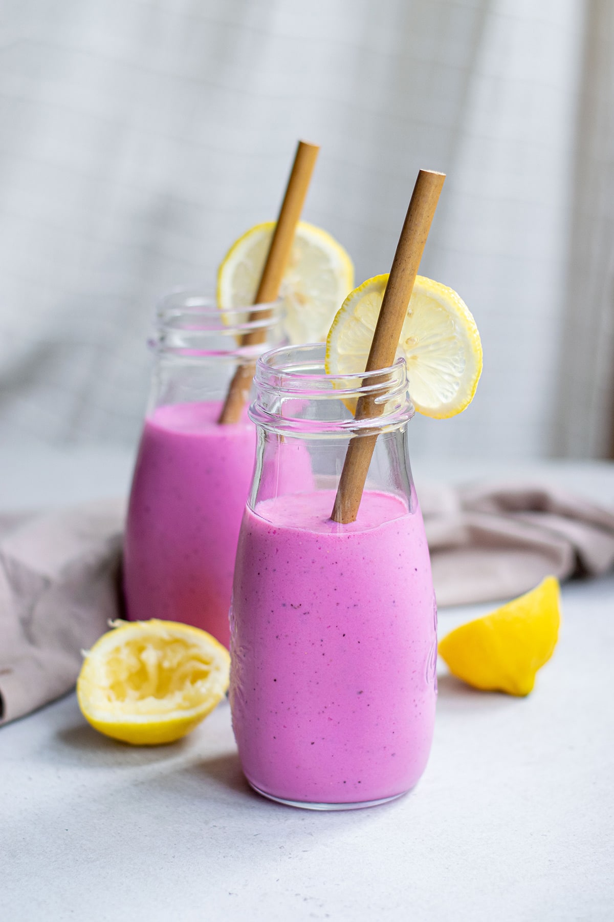 two glass jars filled 3/4s of the way with pink dragon fruit smoothie with lemons and brown straws.