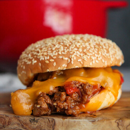 sloppy joe sandwich with cheese up close and a red dutch oven in the background.