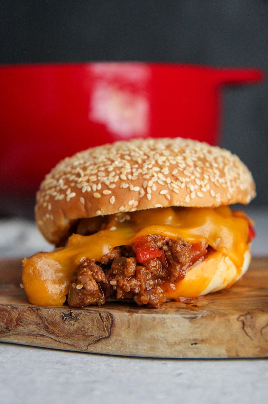 sloppy joe sandwich with cheese up close and a red dutch oven in the background. 