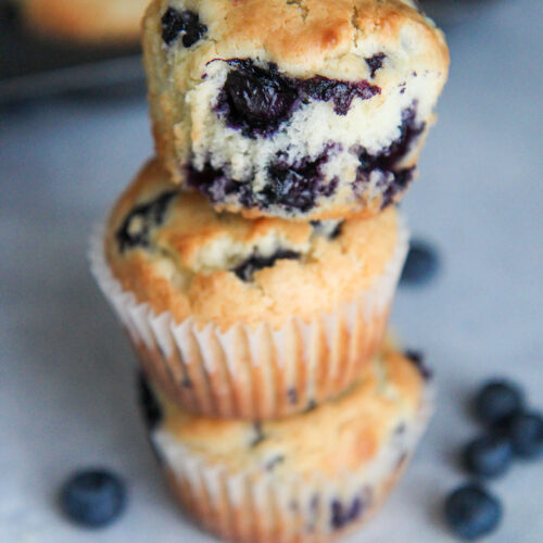 three blueberry muffins stacked with fresh blueberries on the side