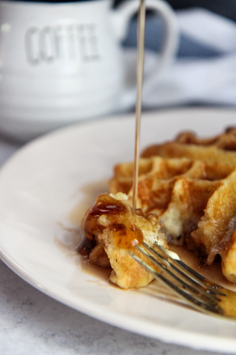 syrup pouring over a piece of waffle with a fork on the side. 