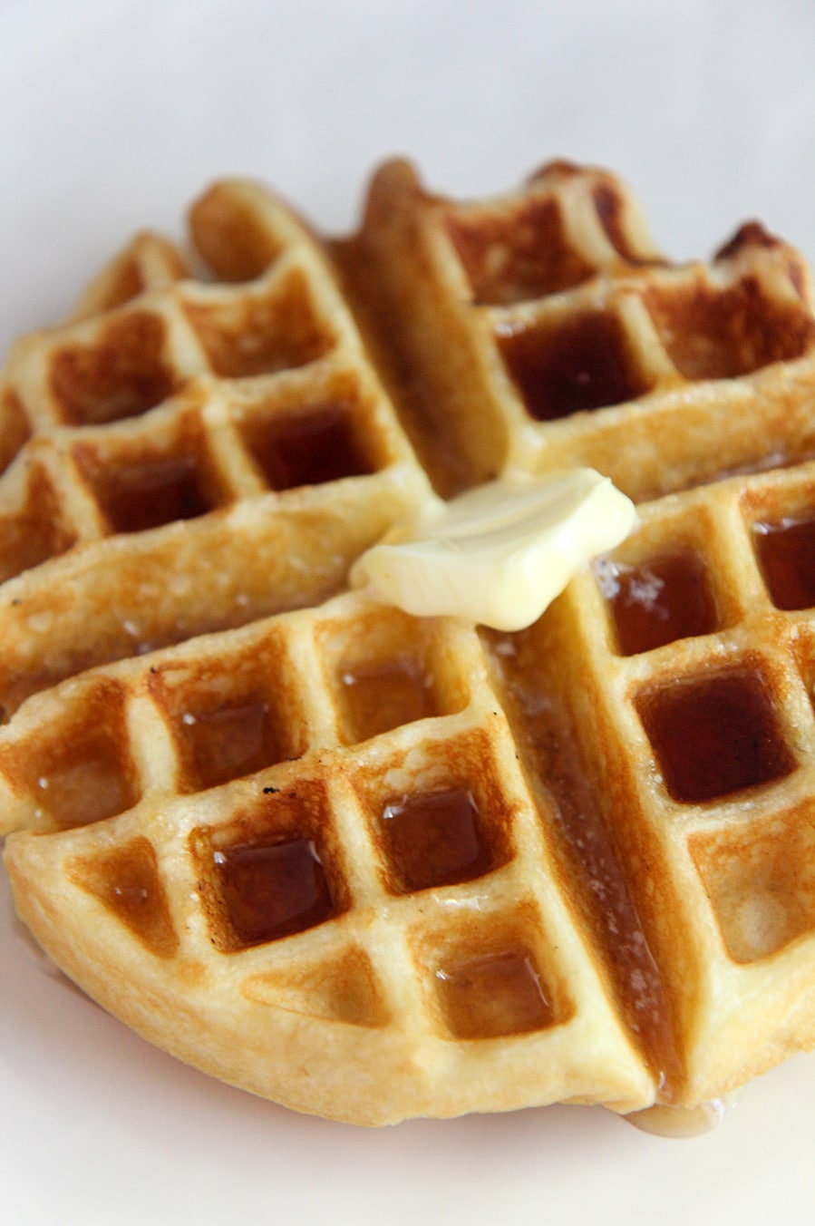 buttermilk waffle with syrup and butter on a white plate up close.