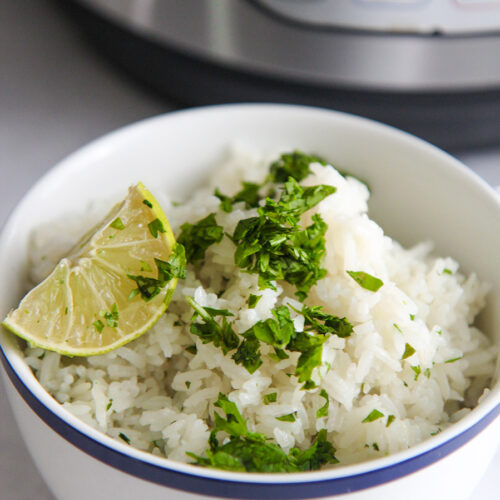 a blue and white bowl filled with fluffy rice, a lime wedge, and cilantro.