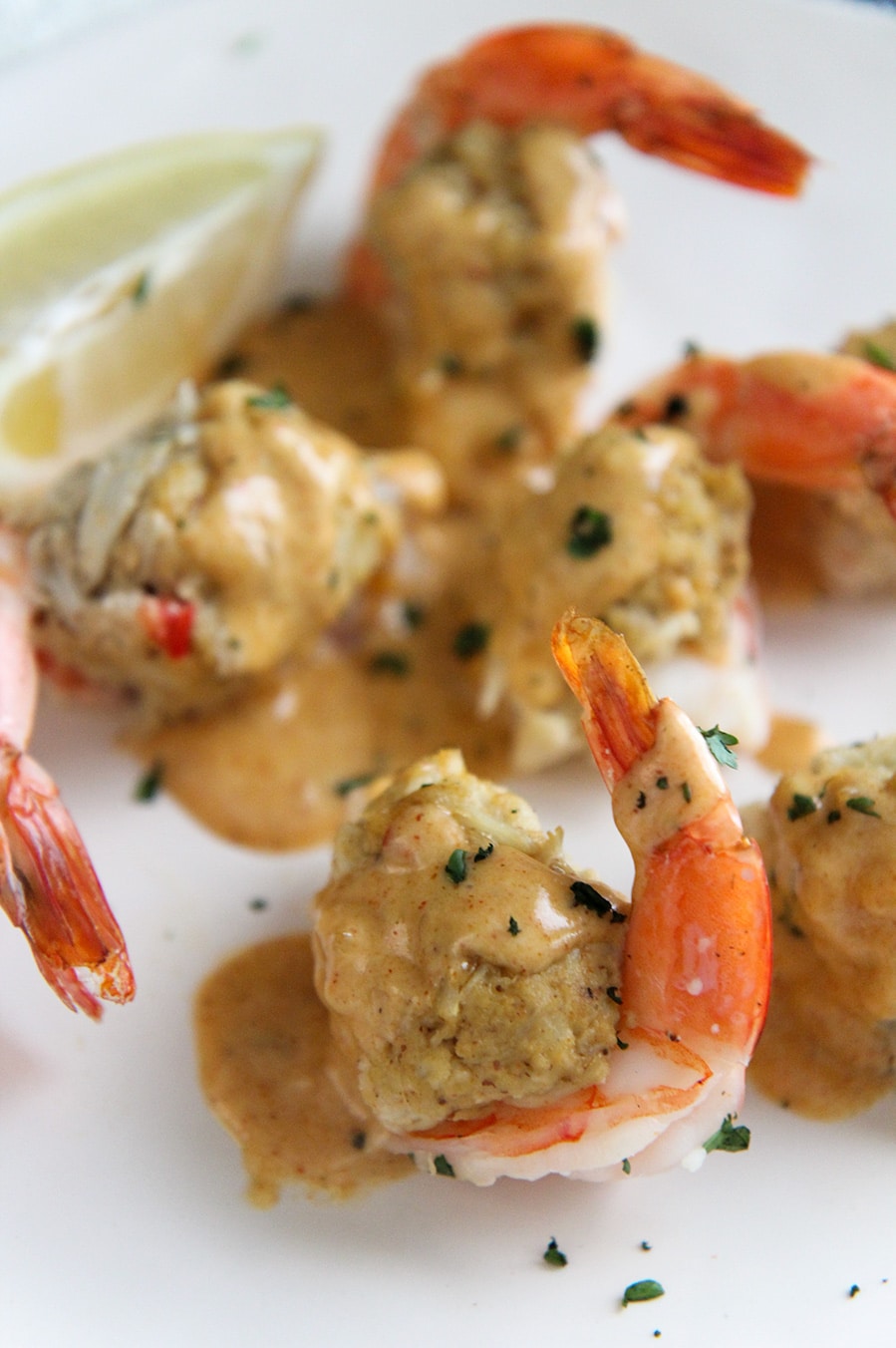 crab stuffed shrimp up close with sauce and a lemon wedge on the side. 