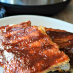 two racks of bbq ribs on a white plate up close.