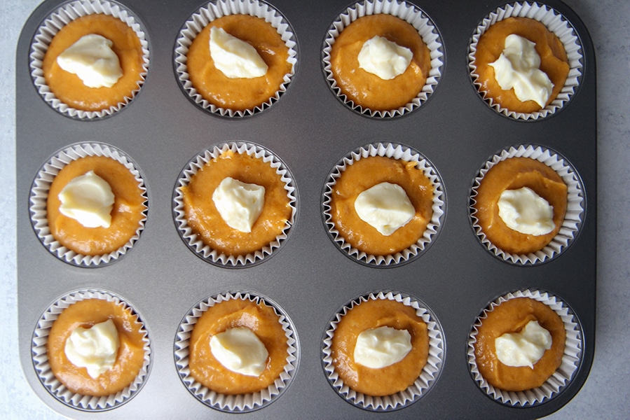 a muffin tin with 12 cupcake liners filled with muffin batter and cream cheese filling. 
