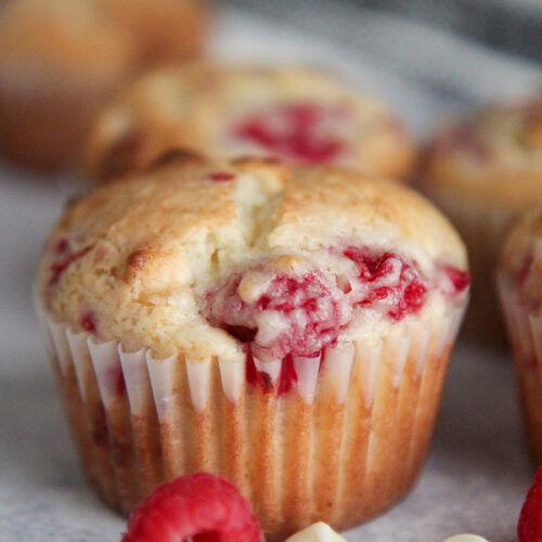 a muffin up close with ra raspberry and white chocolate chips on the side.