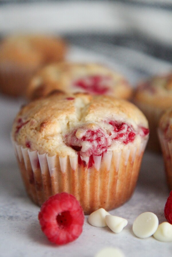 a muffin up close with ra raspberry and white chocolate chips on the side.