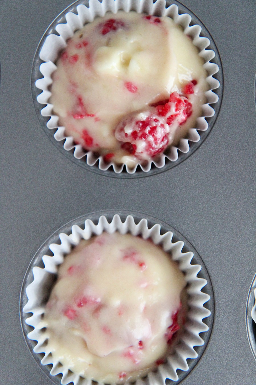 a muffin tin with two cupcake liners filled with batter.