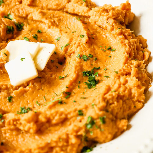 mashed sweet potatoes with butter and green herbs on top.