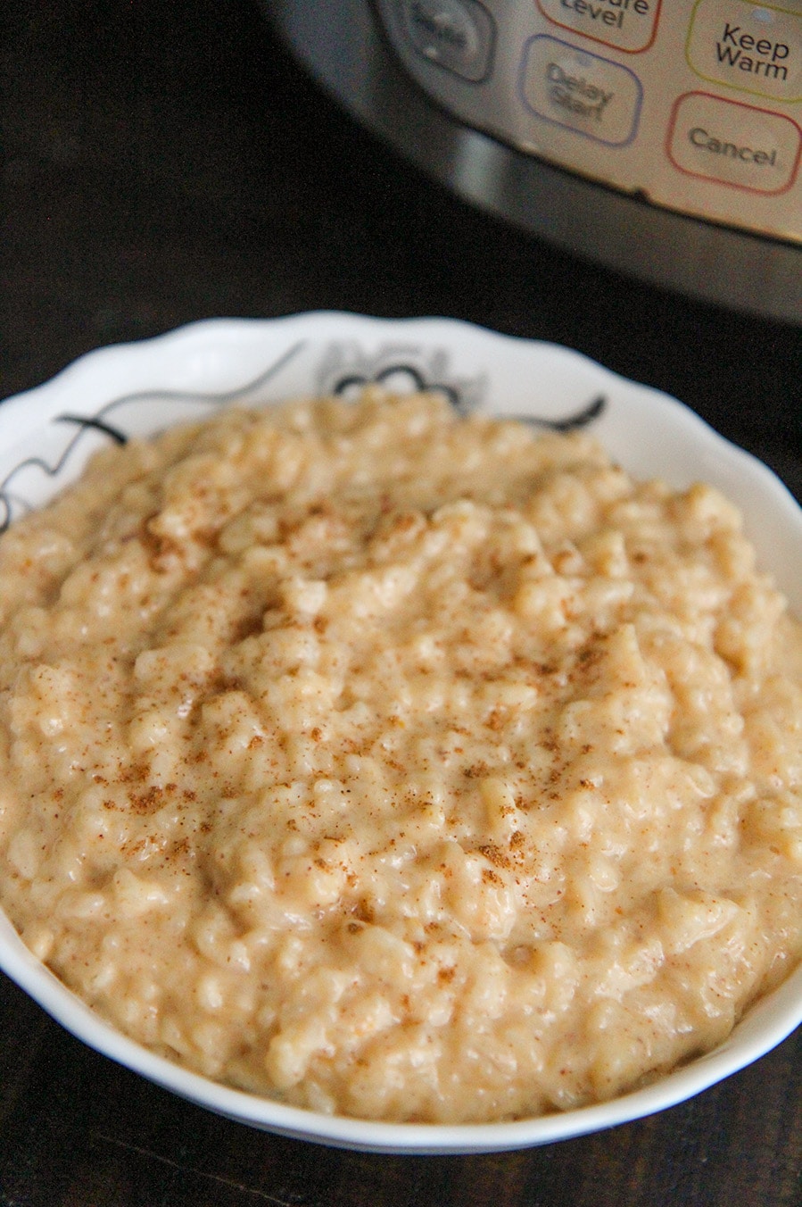 a white bowl filled with rice pudding and an instant pot in the background. 